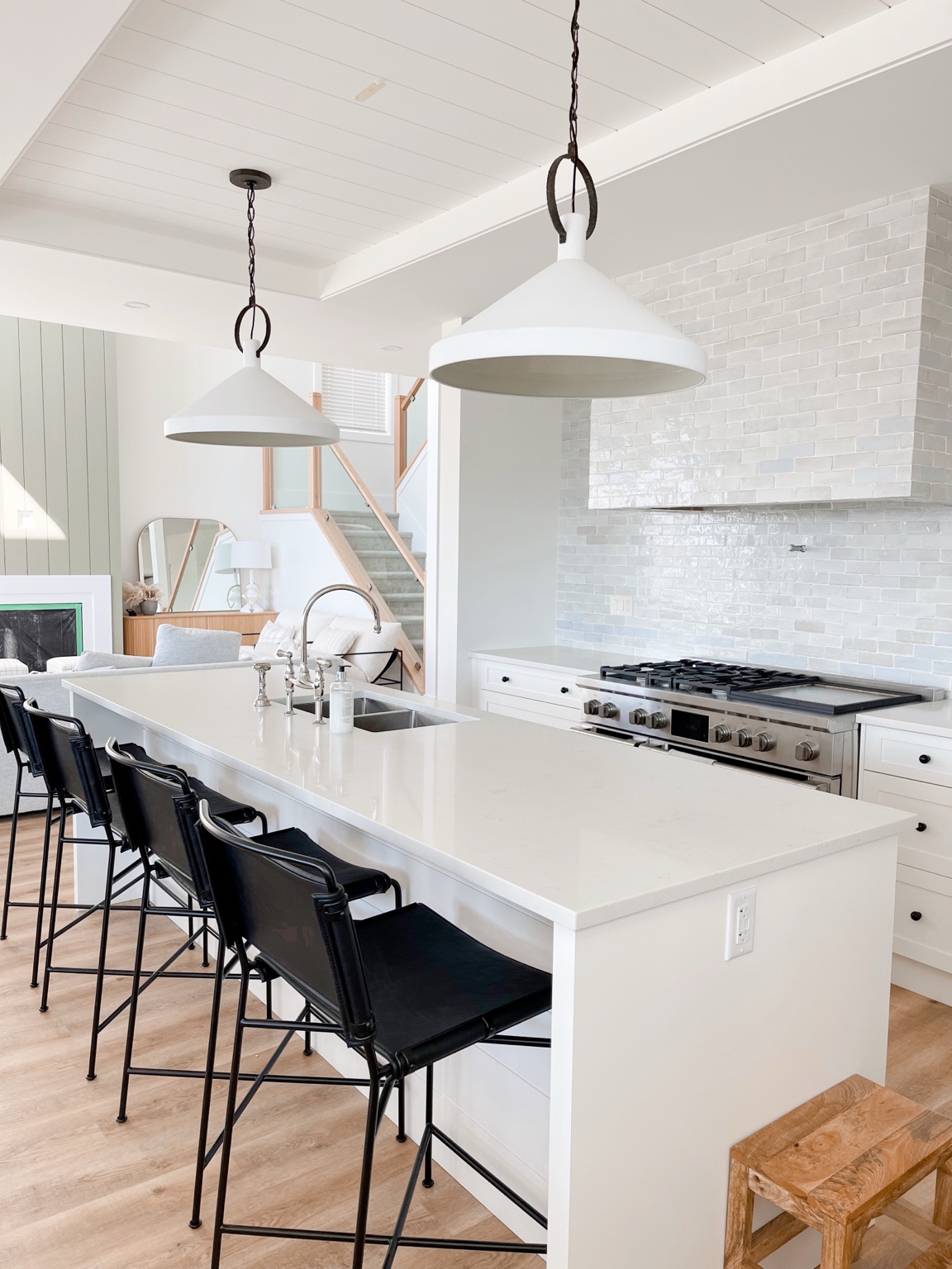 White kitchen with a long island, black stools, and pendant lights by Keystone Kitchen & Bath